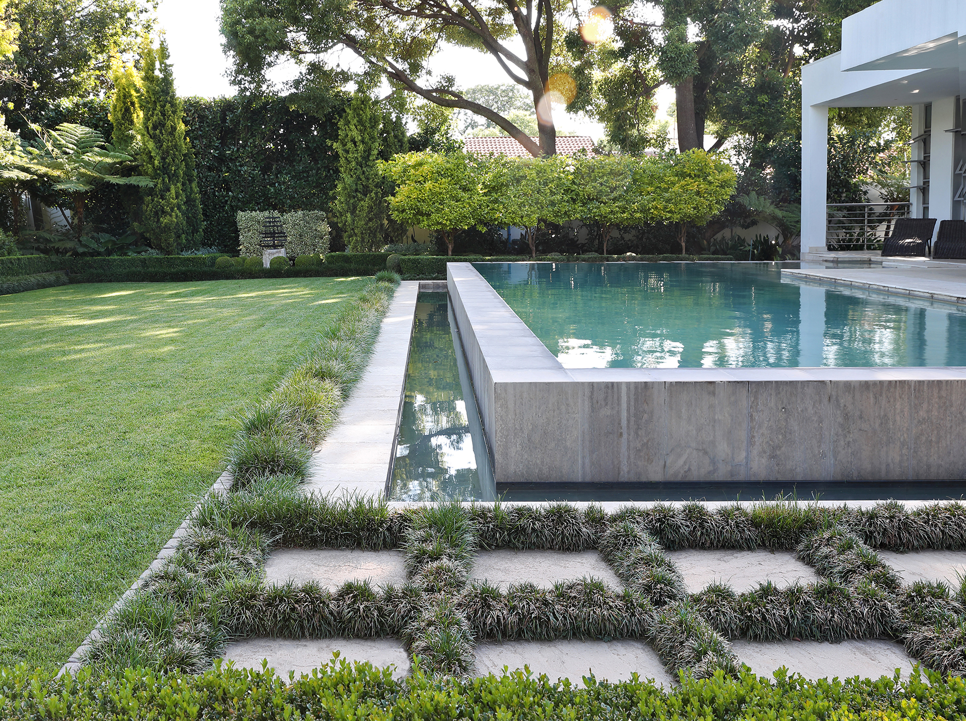 Beautiful image of a formal garden with large lawn, raised concrete swimming pool and planted paving stones, created by Young Garden Design.