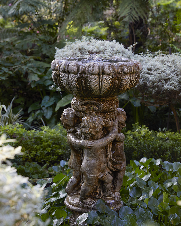 Water feature of three cherubs holding up a concrete bowl with overflowing water, by Young Garden Design